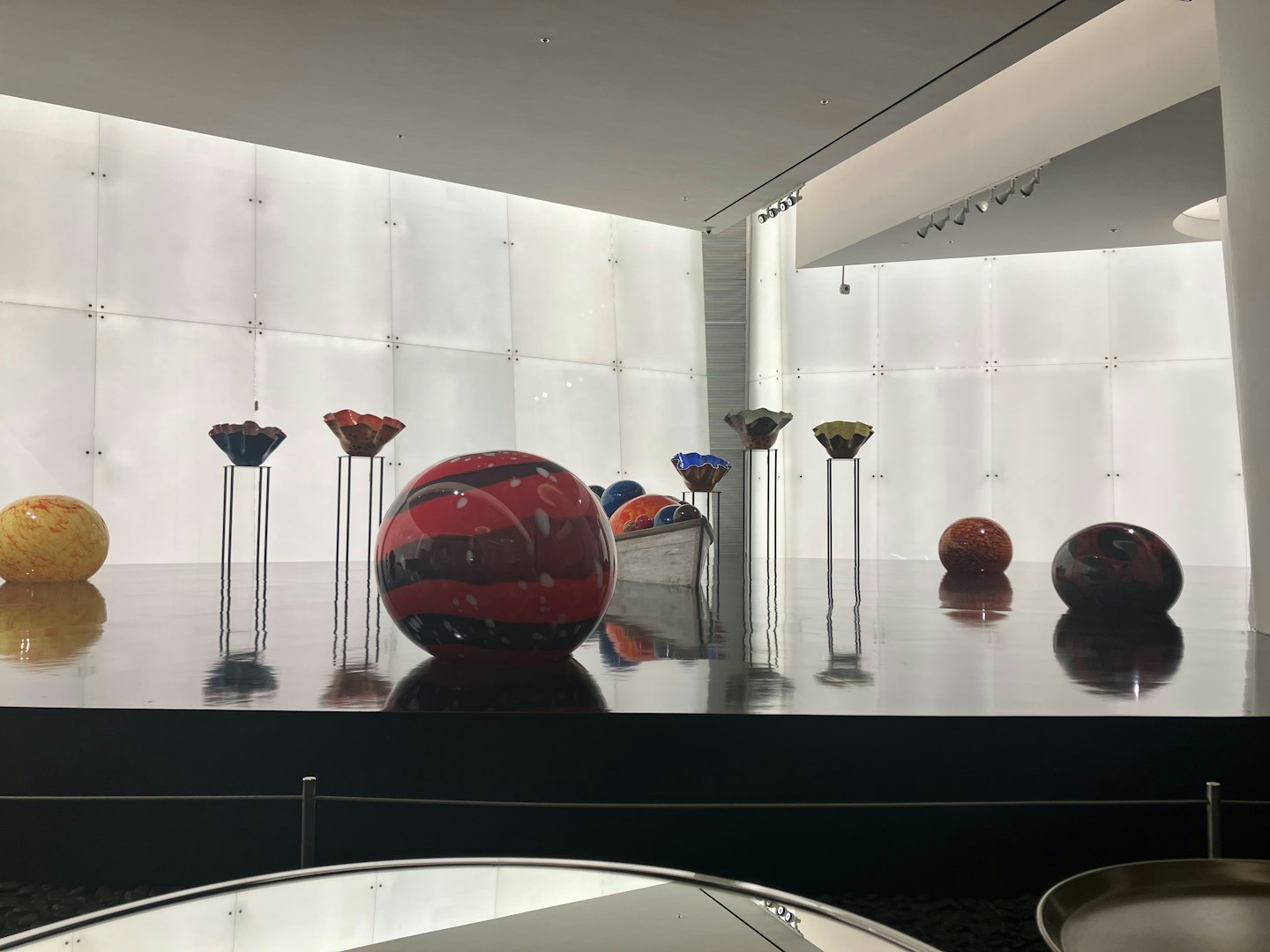 Bunte Glasskulpturen auf reflektierendem Boden in einer Galerie.